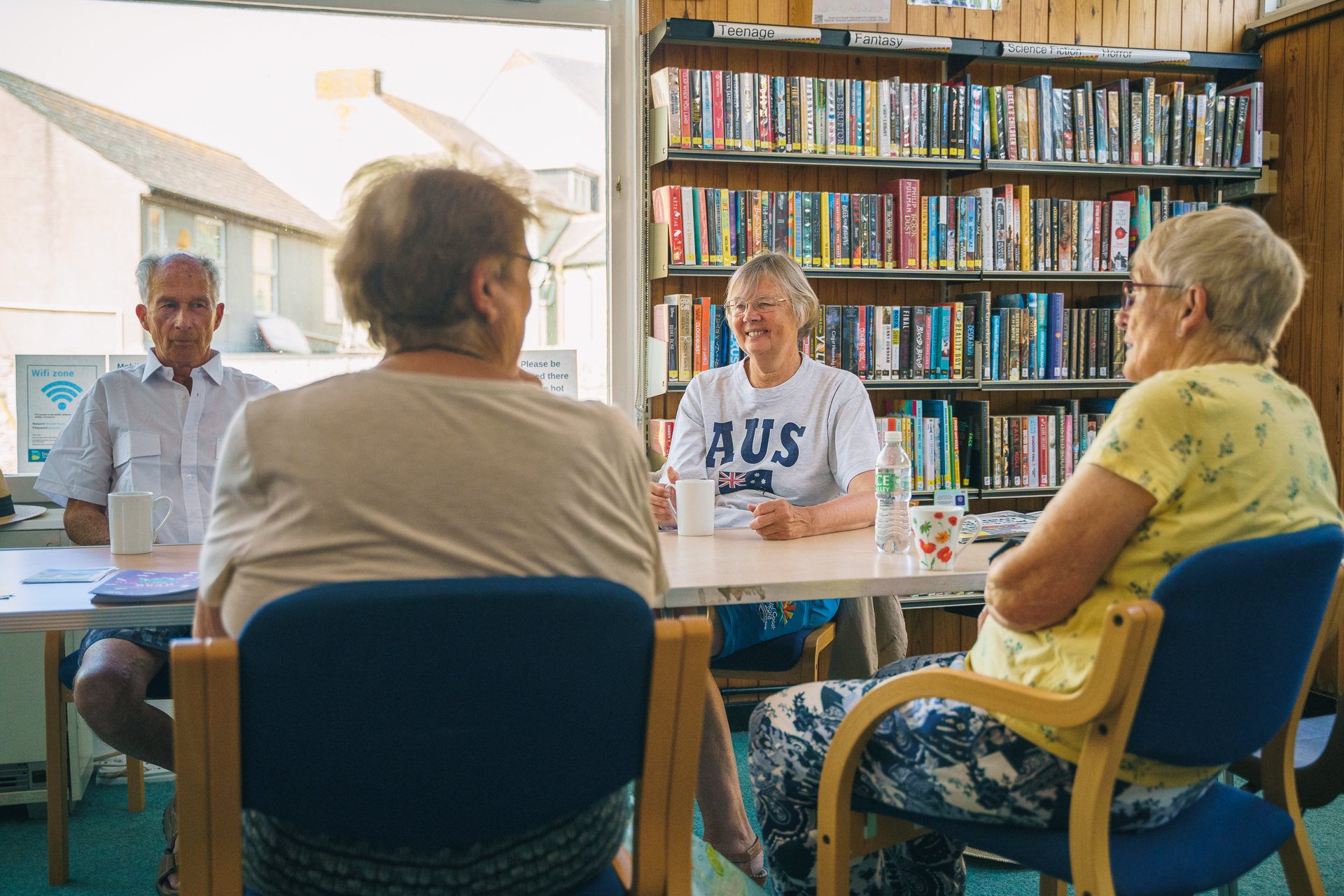 An image of four older people sat around a table in a library, smiling and talking.