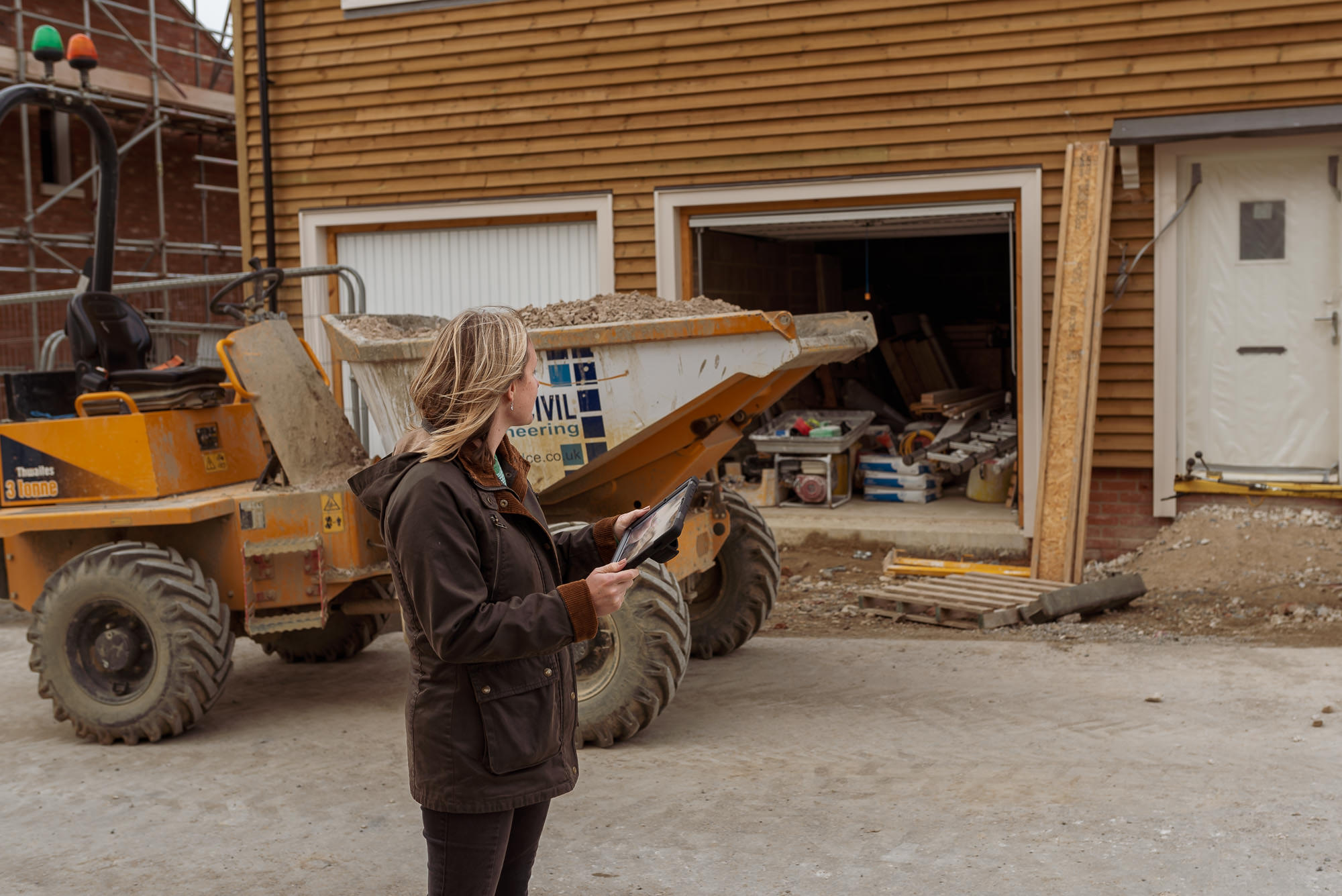 Woman with a tablet looking at a part built house. There is a vehicle to the left of shot.