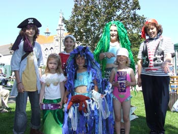 7 children in fancy dress. There are pirates and mermaids. One child is holding a box of chocolates. 
