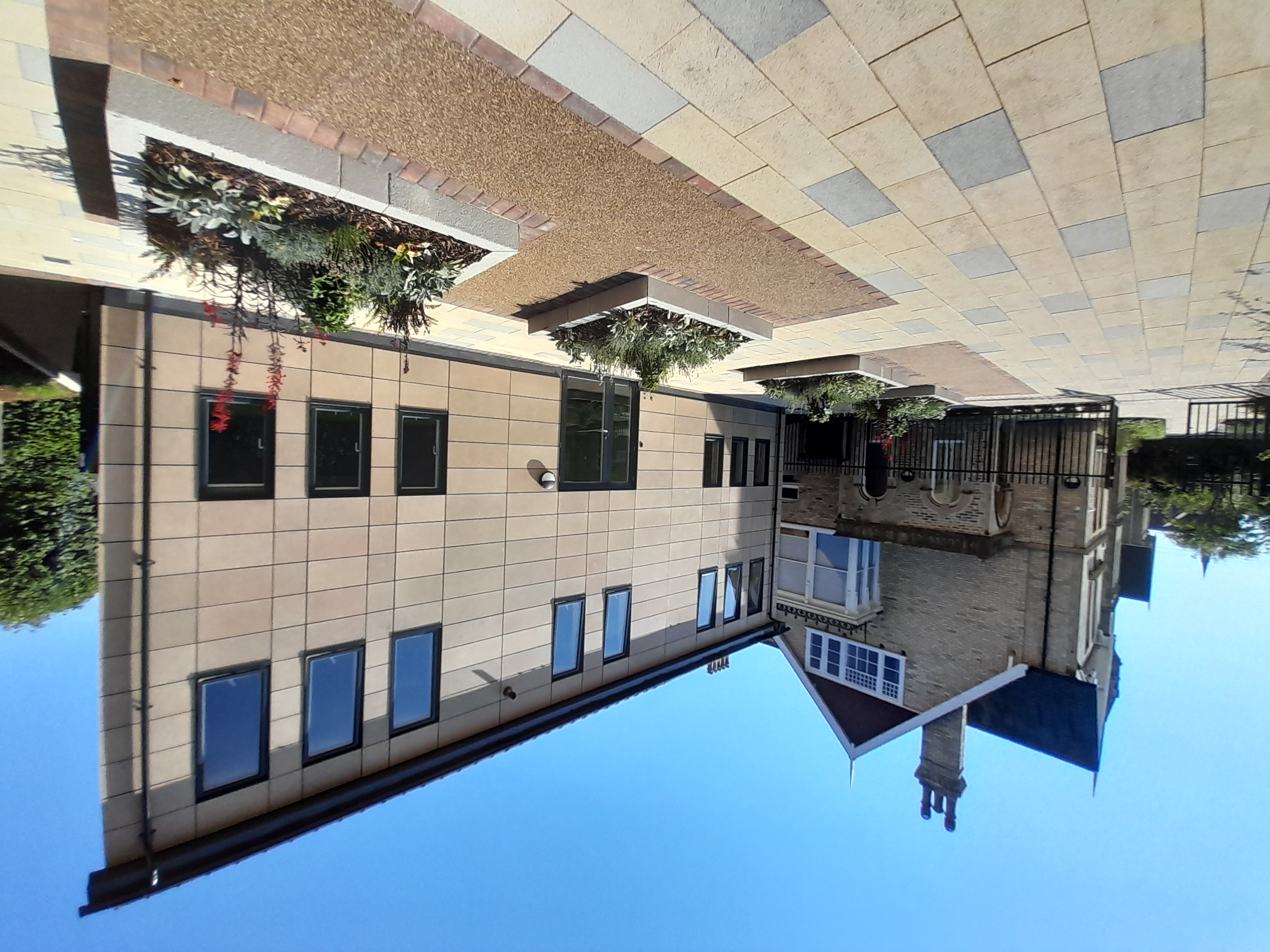 Courtyard with two buildings: an older stone building with a chimney and bay window on the left, and a modern beige-paneled building with multiple windows on the right.