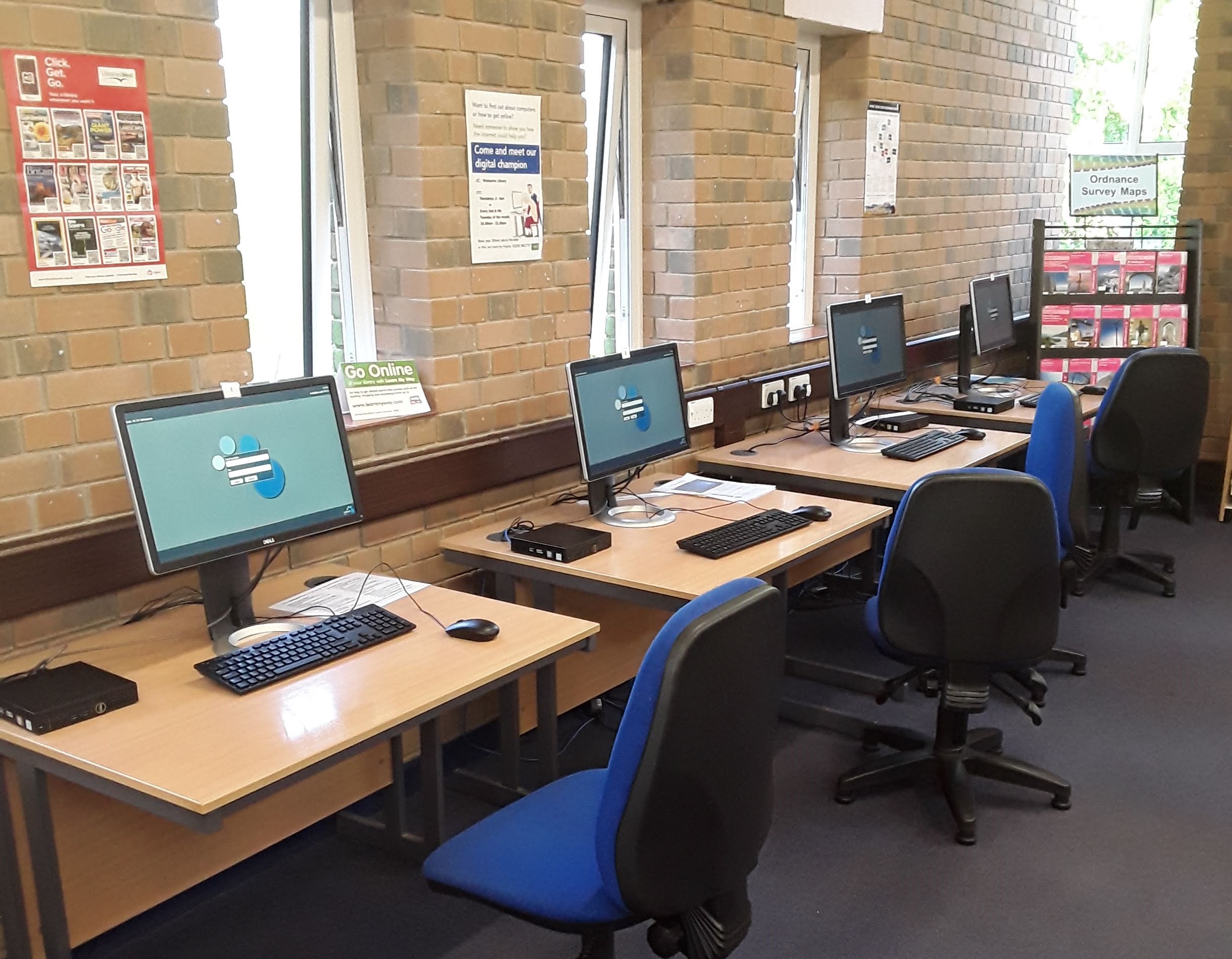 Picture of 4 computer desks with blue chairs. Each desk has a public use computer on it showing the log in screen.