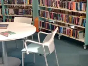 This is an image of a white table and two chairs.  There are some books on the table and shelves of books in the background.