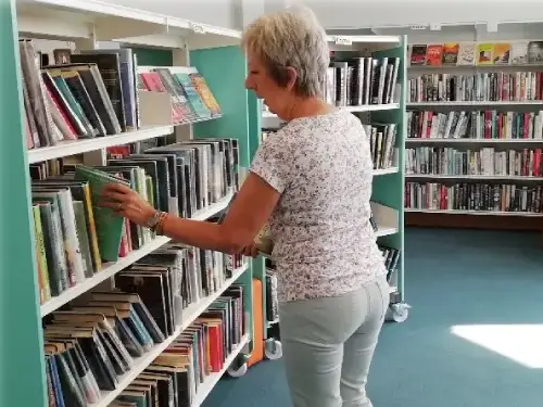 This picture shows a person pulling out a book from a shelving unit full of books.