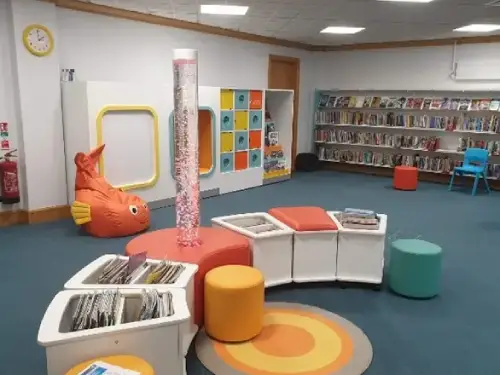 This is a picture of the children's area with bubble tubes and fish shaped bean bag in the background.  There are book holders and seats for children in the foreground.