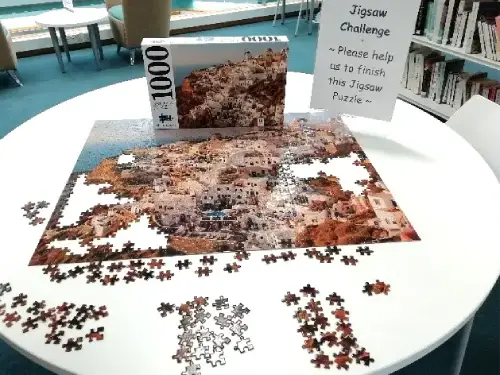 This picture shows a table with a jigsaw puzzle half completed on it and the puzzle box in the background. There is a notice saying, Jigsaw Challenge beside the box.