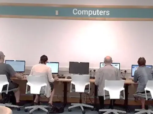 This picture shows four people sitting on chairs looking at computer screen, there is one computer in the middle unused.