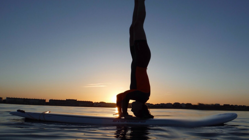 Young women doing a head stand on a stand up paddleboard in Portland