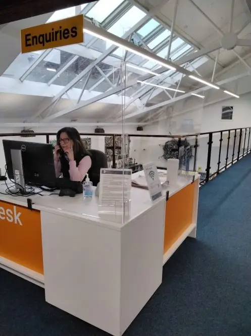 This is a picture of a front desk and a library assistant sitting behind desk in front of a computer, talking on a phone.