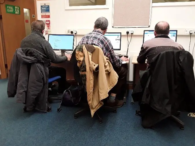 This is a picture of three customers sitting on blue chairs in front of computer screens.
