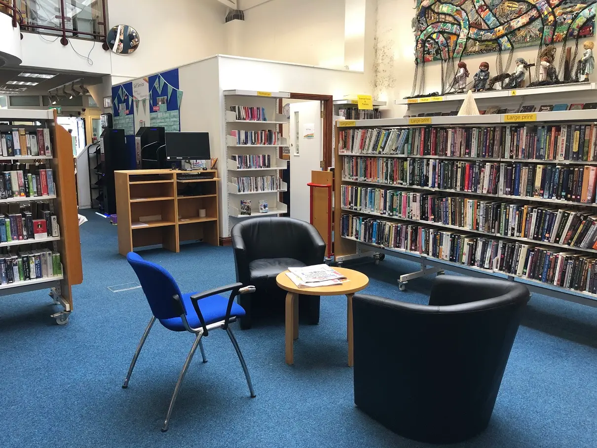 This is a picture of shelves of books to the left and two chairs and a table to the foreground.