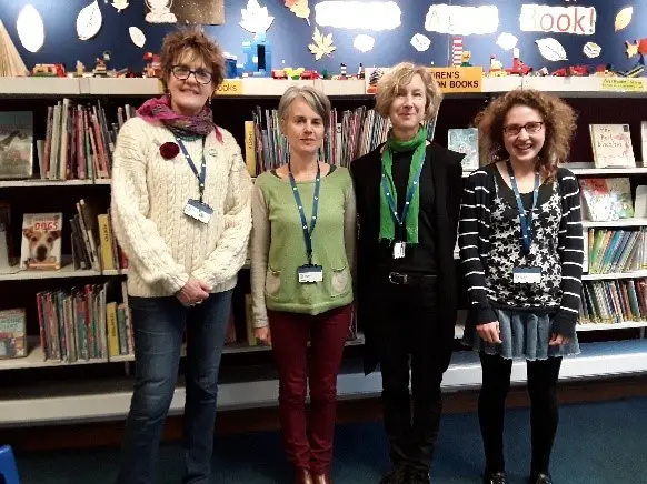 This is a picture of four library assistant standing looking and smiling at the camera.