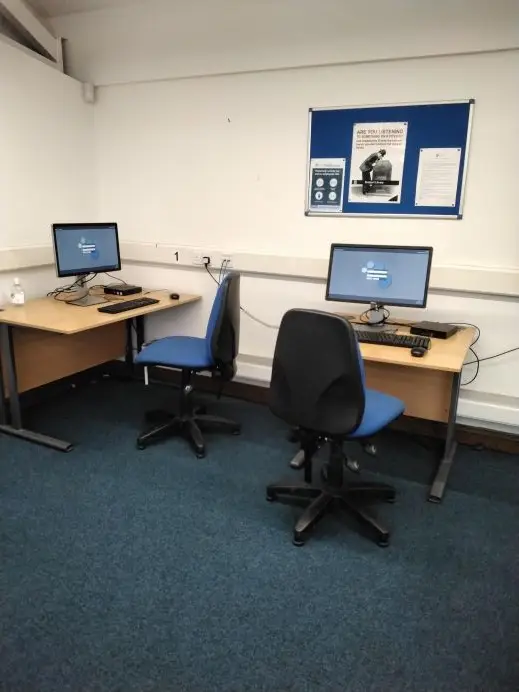 This is a picture of two desks on which sit a computer and keyboard and a blue chair in front of each desk.