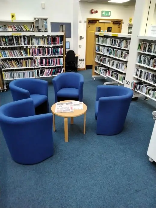 This is a picture of four blue chairs around a small wooden table with shelves of library books in the background.