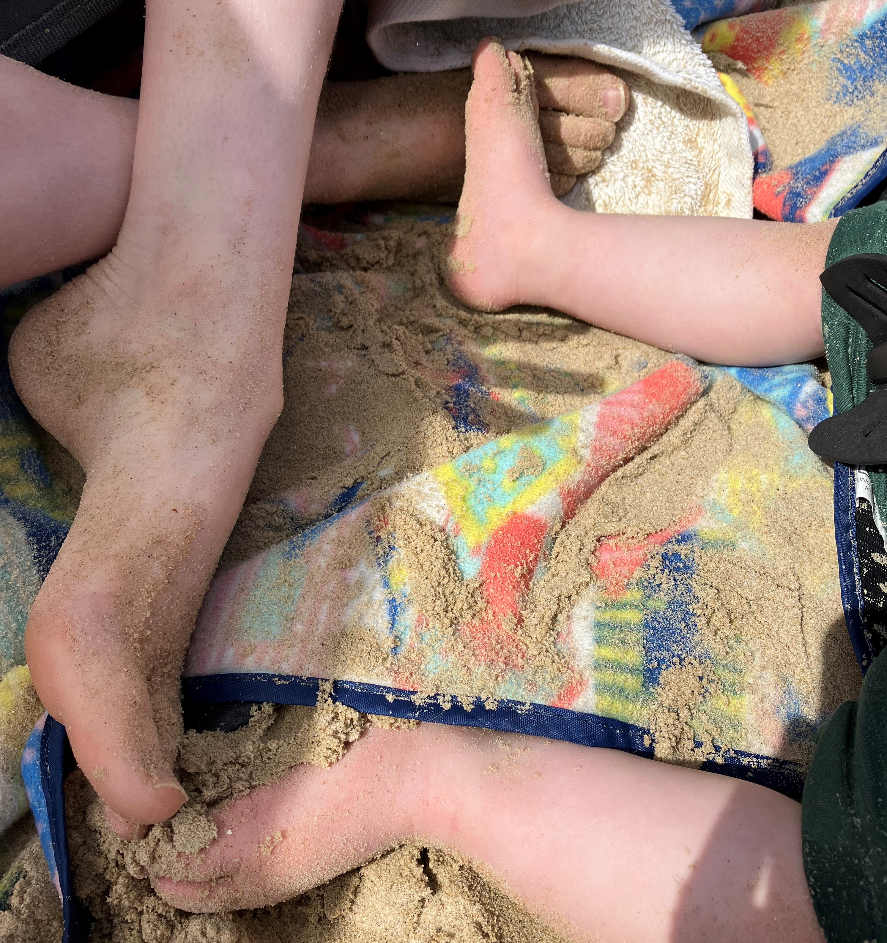 a young person's foot and baby feet on a beach towel