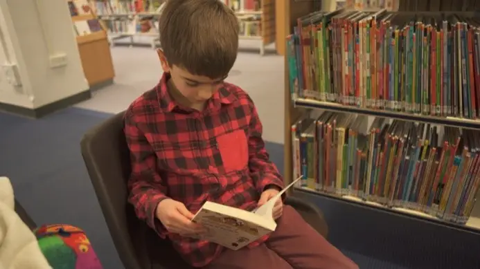 This is a picture of a child sitting in a chair, reading a book.