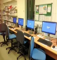 This is a picture of a row of desks with computer screens and keyboards on each and chairs in front.