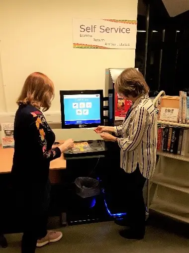 This is a picture of a library assistant helping a customer to use the self service machine.