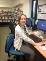 This is a picture of a library assistant sitting in front of one of the computers ready to help a customer.