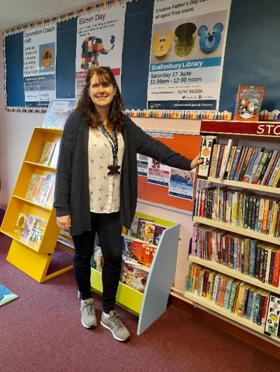 This is a picture of a library assistant standing in front of shelves of books.