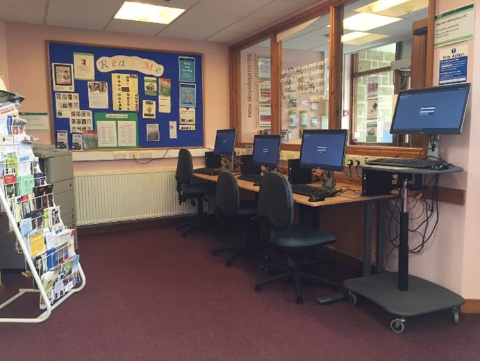 This is a picture of three desks with computers and keyboards and chairs in front.  There is also one higher desk to stand at with computer screen and keyboard.