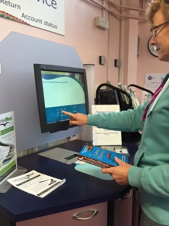 This is a picture of a library assistant checking out a book on the self service machine.