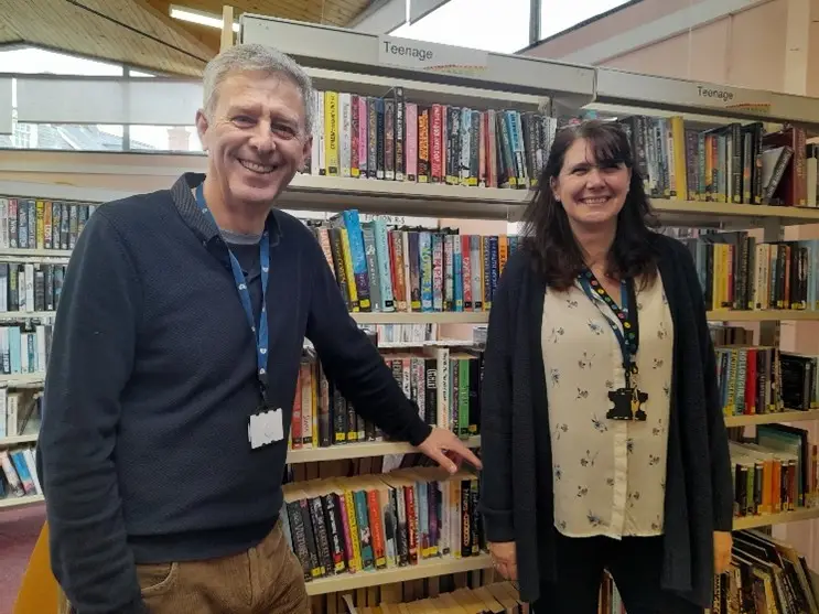This is a picture of two library assistants standing looking at the camera and smiling.