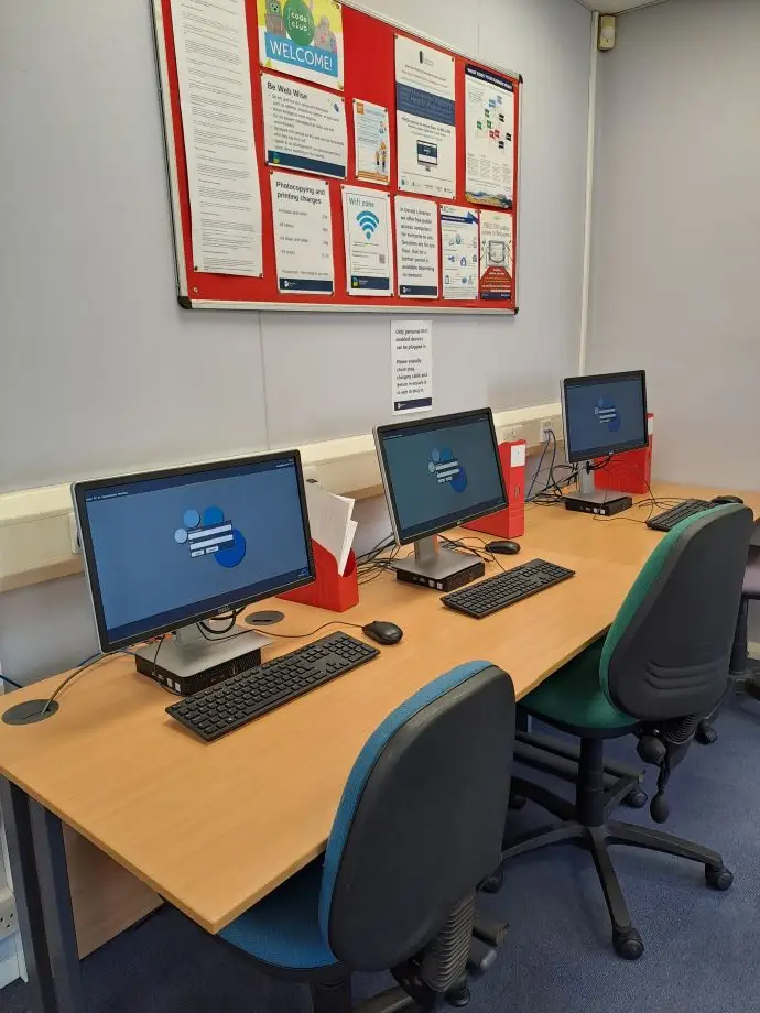 This is a picture of a long desk with three computer screens and keyboards with chairs in front.