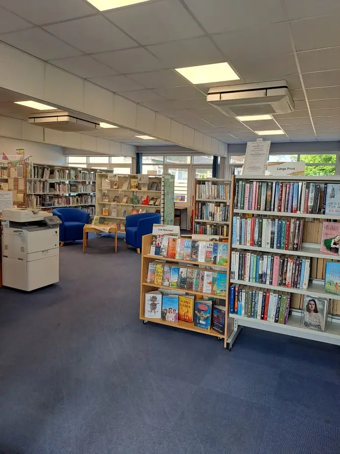 This is a picture of shelving units full of books with a table and chairs in the background.