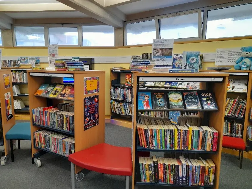 This is an image of rows of shelves filled with books with a red stool between shelves.