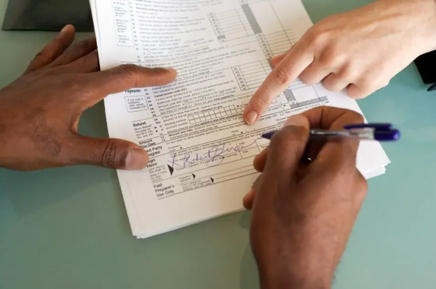 This is a picture of a person filling in an application form with a library assistant helping them.  The picture only shows the peoples hands.