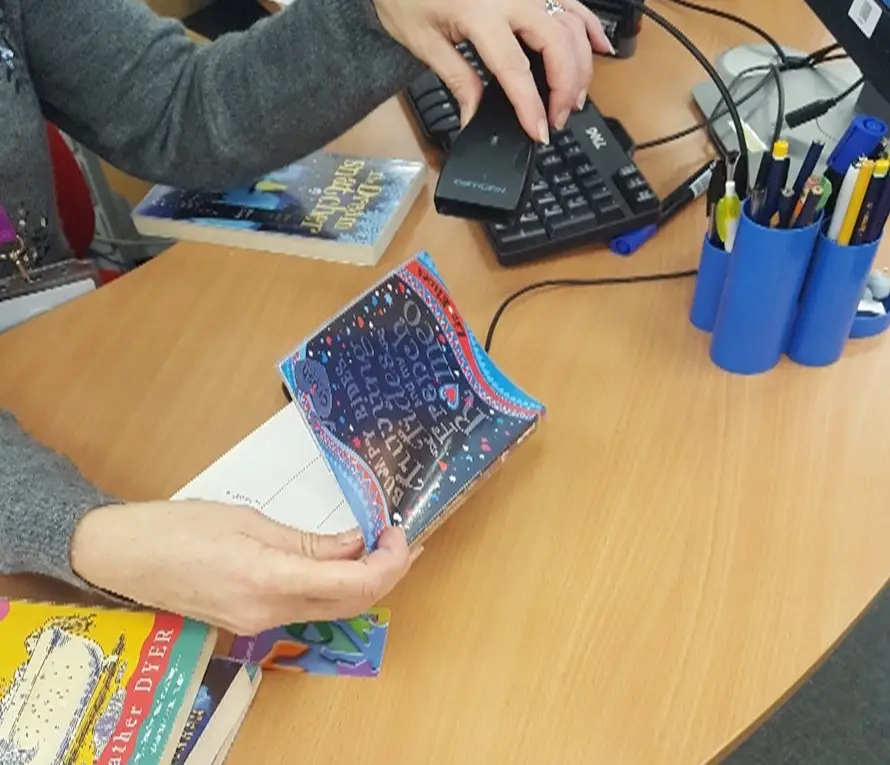 This is a picture of a library assistant checking out a book with a hand held scanner.