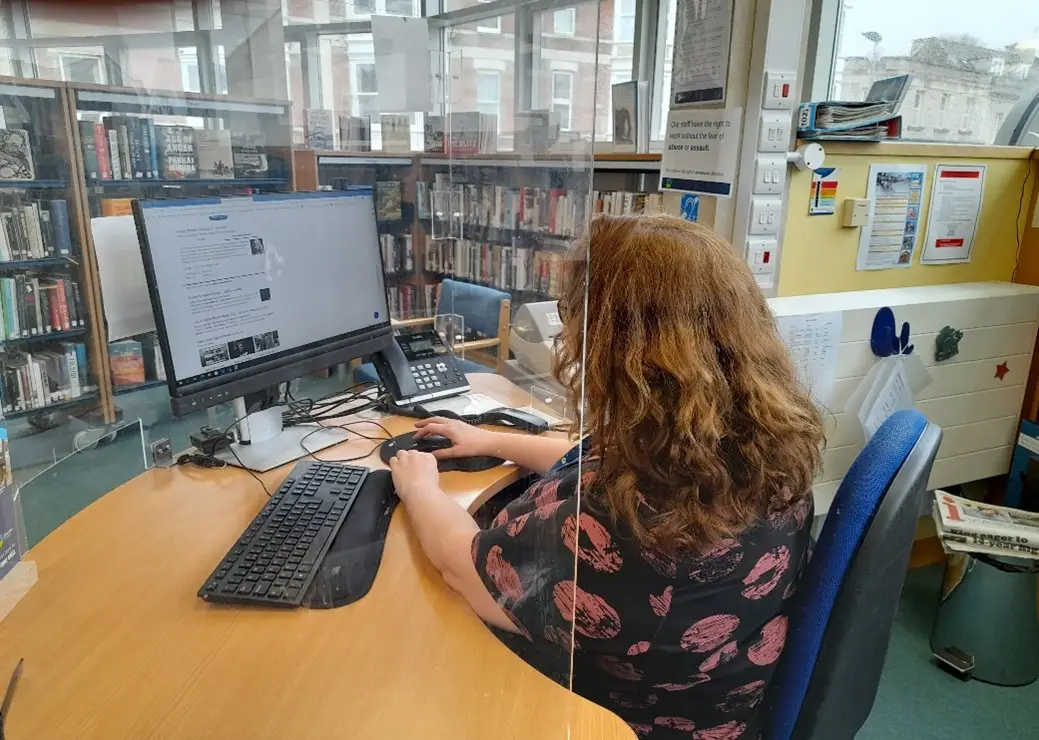 This is a picture of a library assistant sitting behind a desk working on a computer.