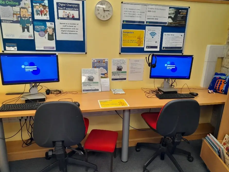 This is a picture of a long desk with two computer screens and keys and two red chairs in front of desk.