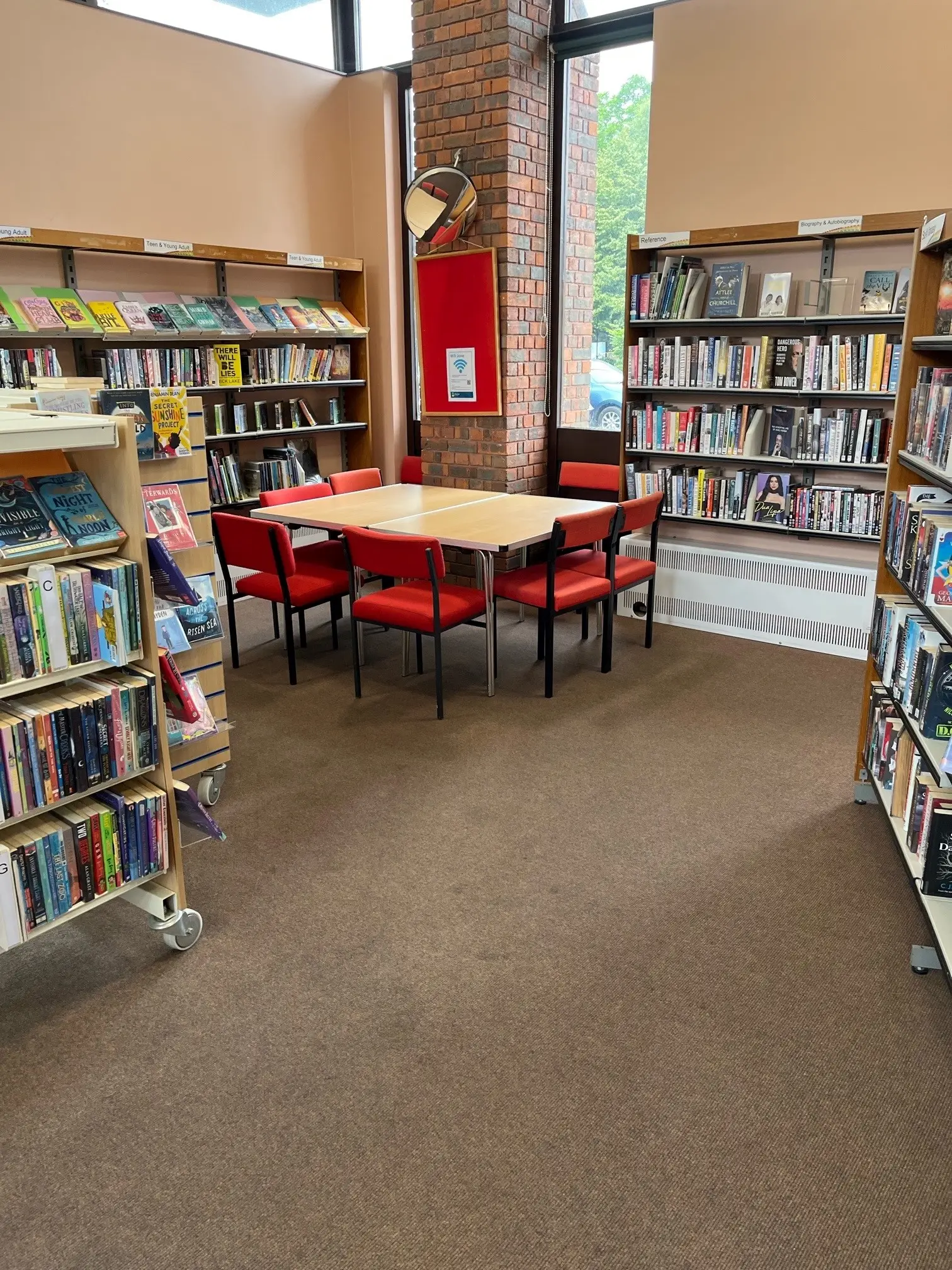 This is a picture of a square table surrounded by seven red chair.  There are book shelves to  the sides and back of the room.