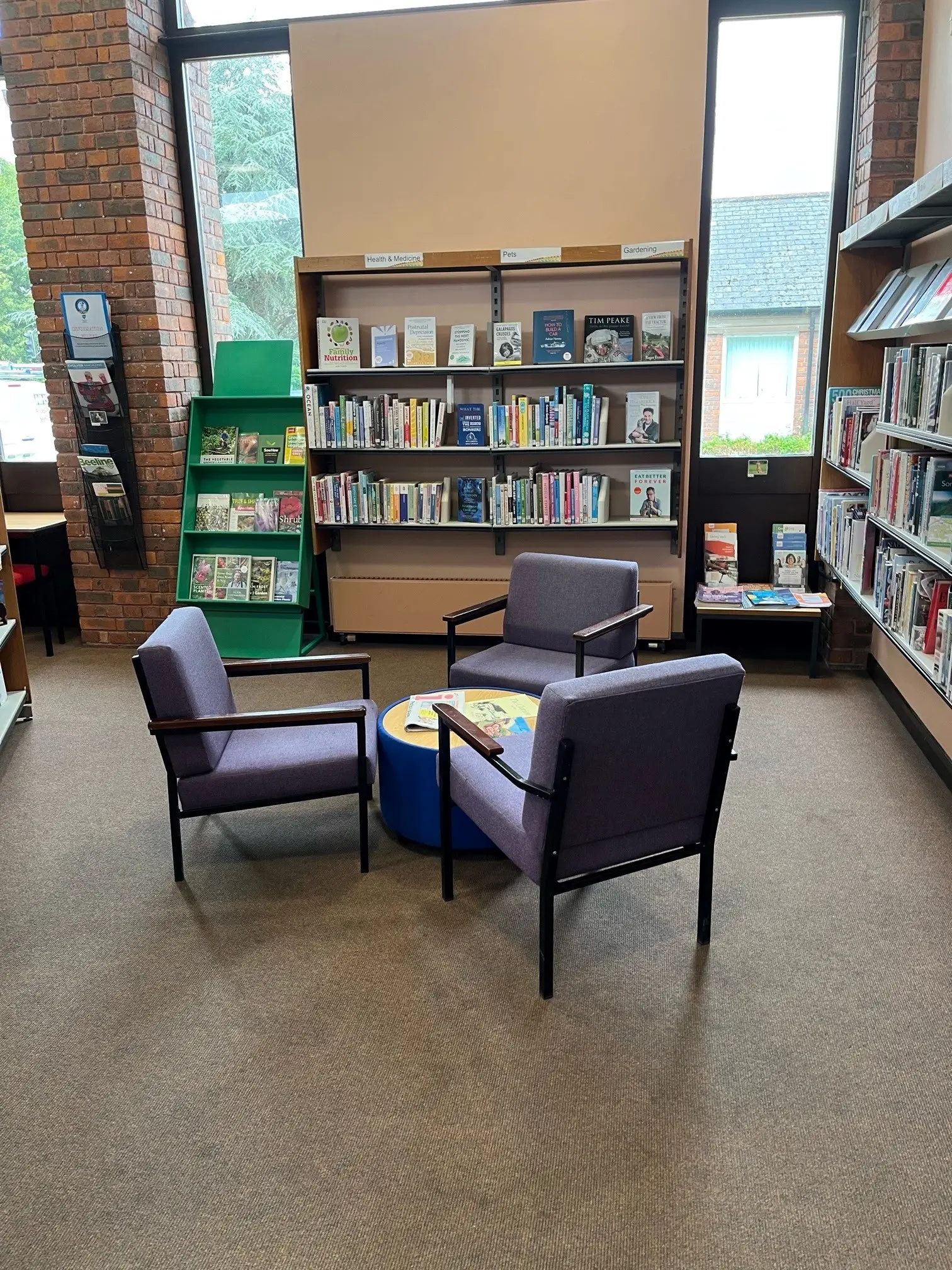 This is a picture of three chairs around a small round table with book shelves to the back and on either side.