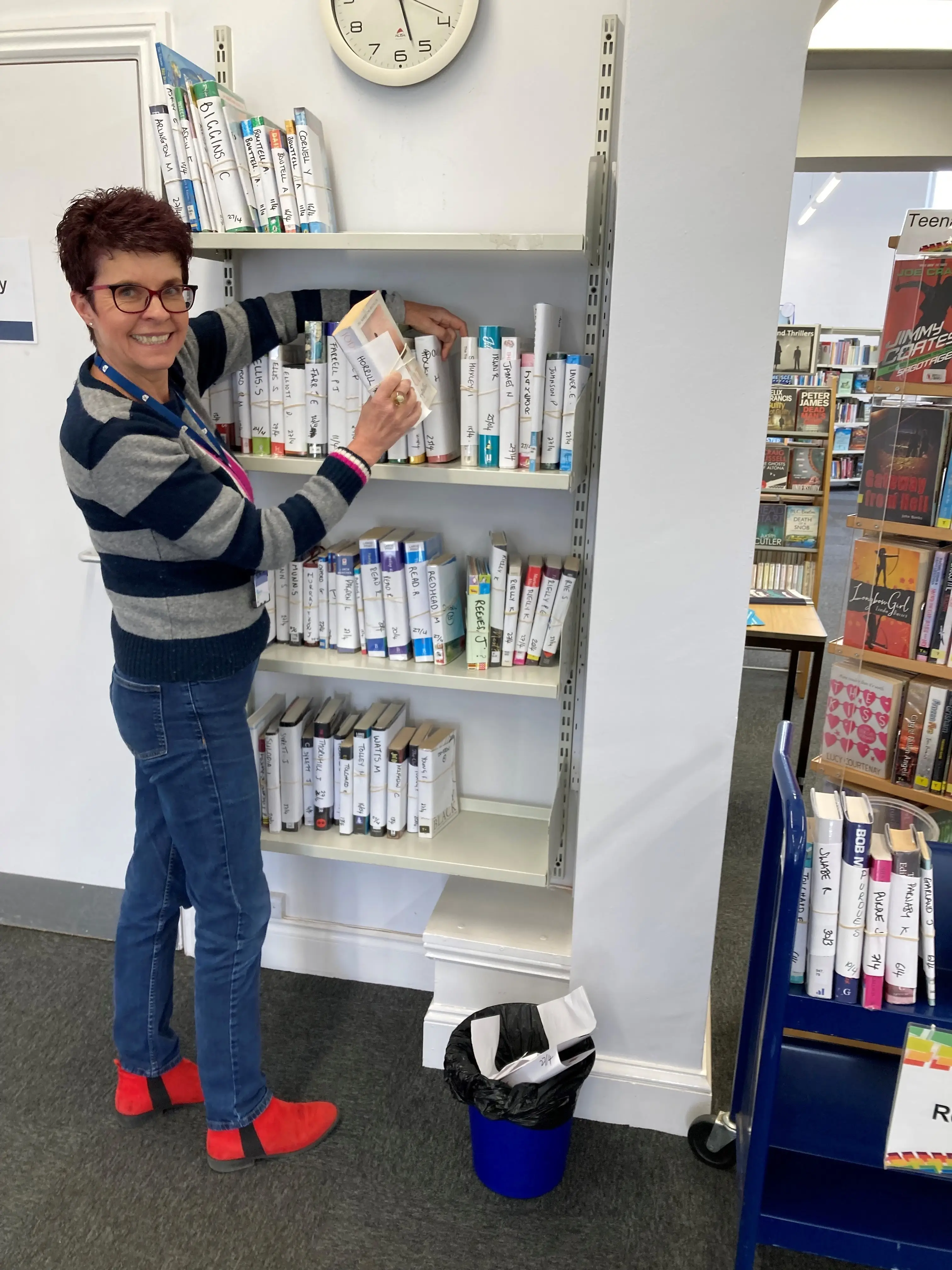 This is a picture of a library assistant putting a reserved book on the shelving unit.