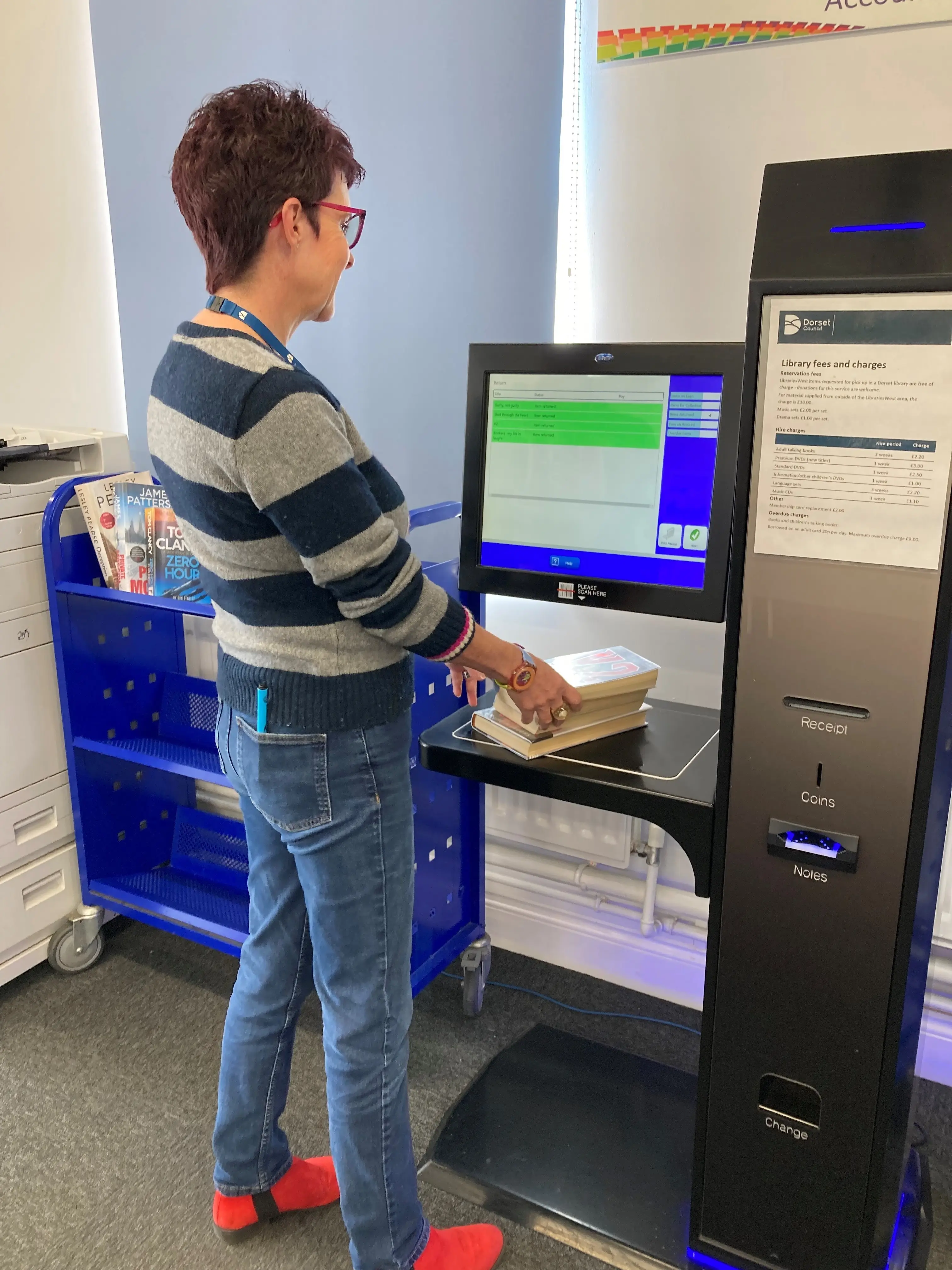 This is a picture of a library assistant helping to check out books with the self service machine.