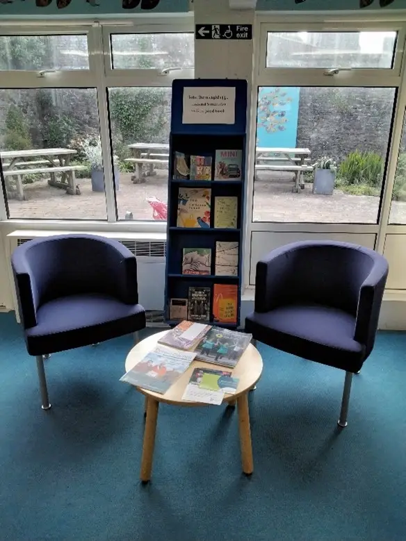 This is the picture of two chairs and a small round table with book display between chairs.