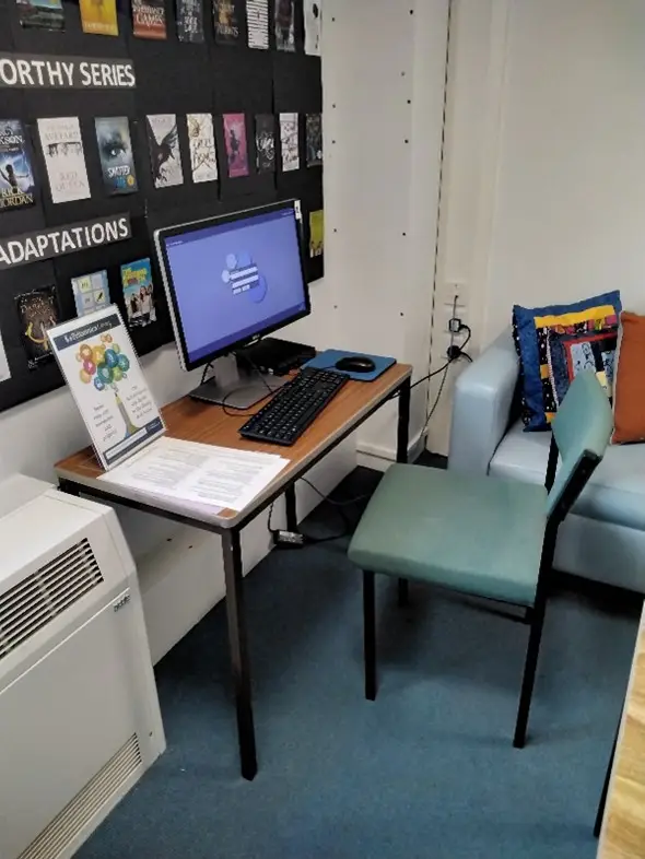 This is a picture of a desk with a computer screen and keyboard and a chair in front.