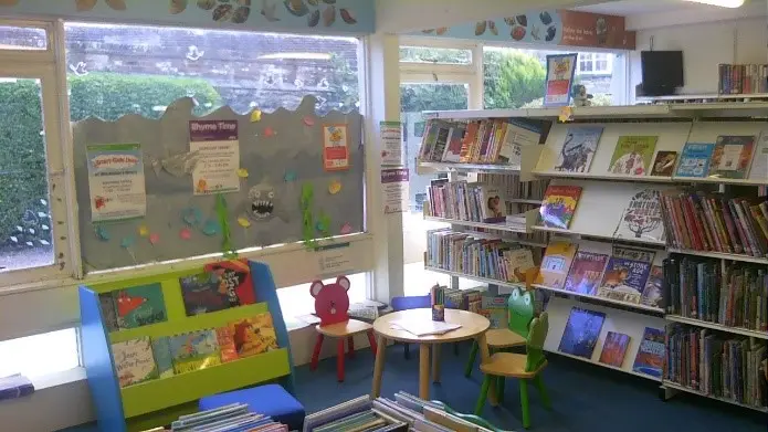 This is a picture of a small round table and three chairs surrounded by shelves of books.