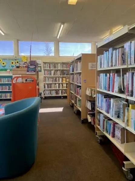 This is a picture of rows of shelves with books and a chair to the left side.