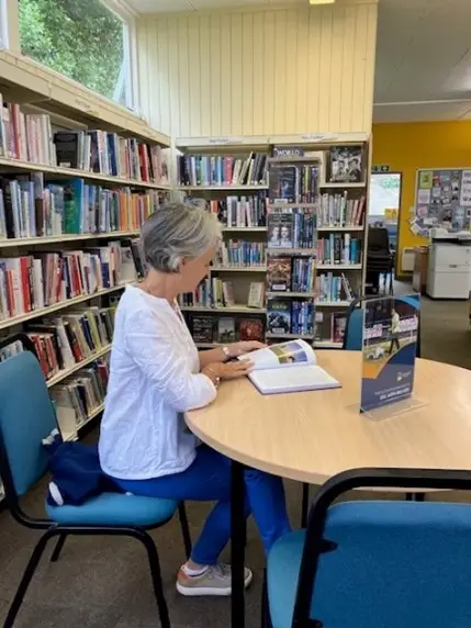 This is a picture of a person sitting reading a book at a found table surrounded by chairs.