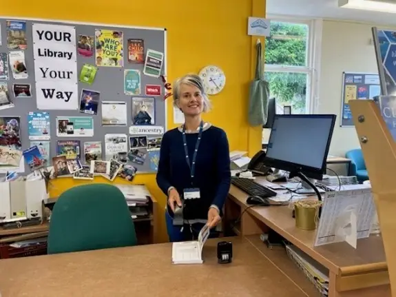 This is a picture of a library assistant behind the front desk smiling at the camera.