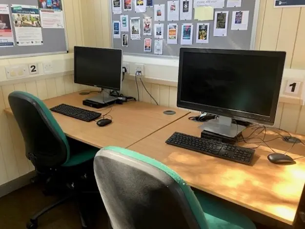 This is a picture of two desks with computer screens and keyboards on the desks.  There are two chairs in front of desks.