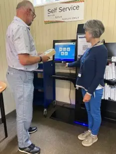 This is a picture of a library assistant helping a person use the self service machine.
