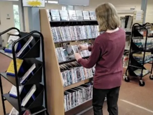 This is the image of a library assistant putting a DVD back on the shelf.