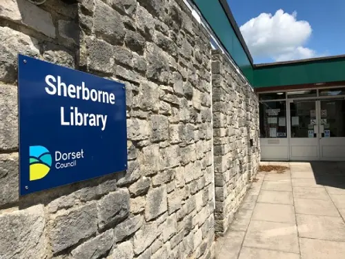 This is an image of the outside of Sherborne Library.  There is a stone wall to the left of image and the front door to the right.