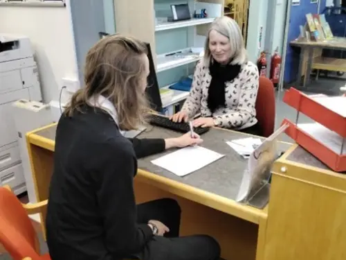 This is an image of a library assistant helping a member of the public to fill in a membership form.