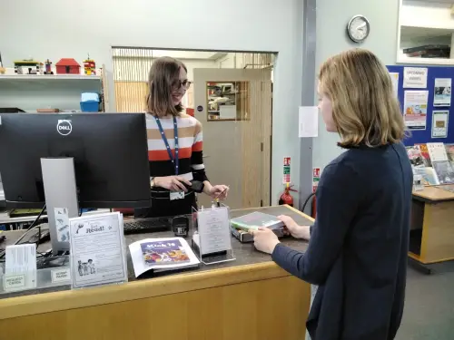 This is an image of a library assistant checking out books for a member of the public.