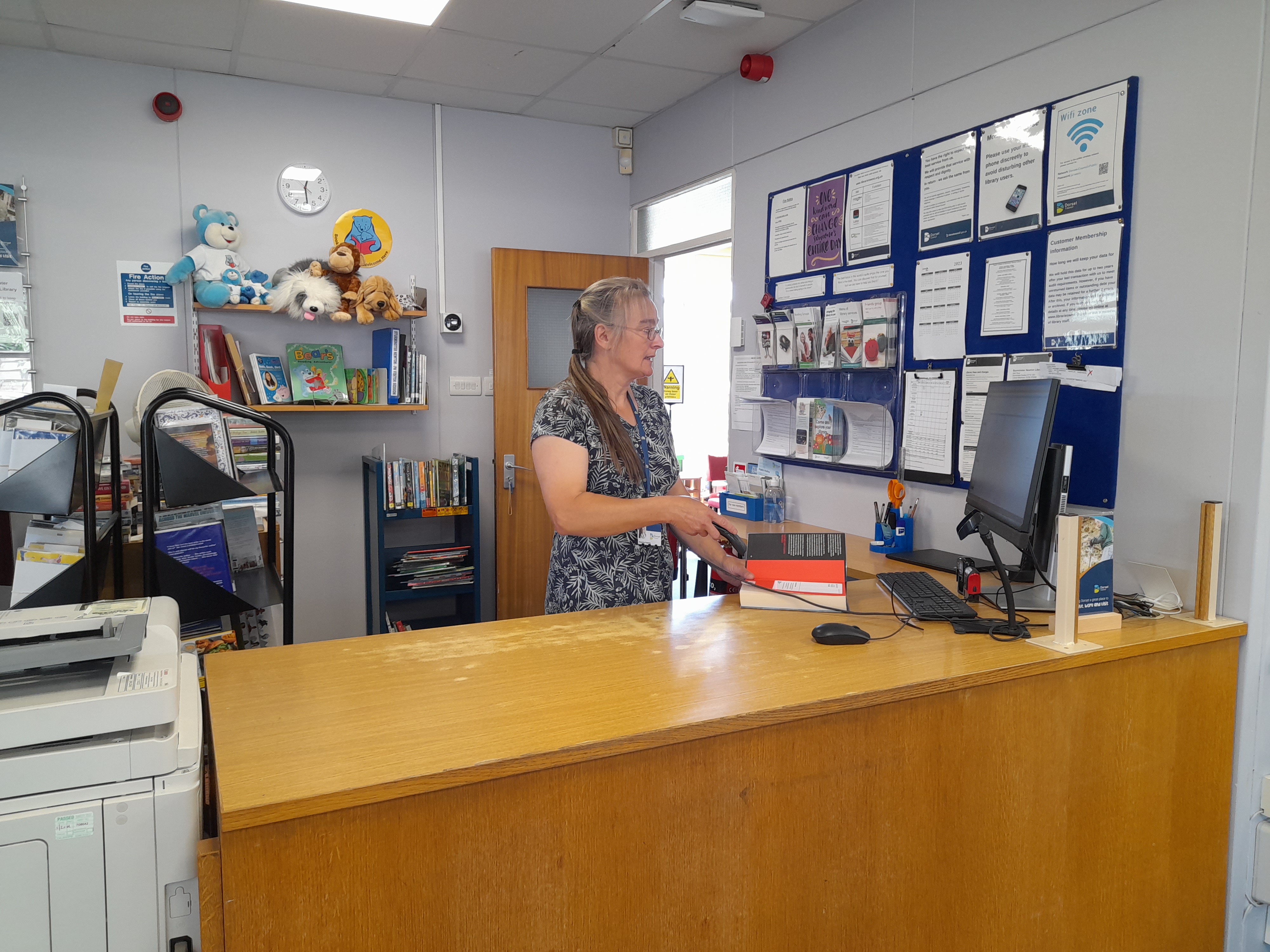 This is an image of a library assistant behind the front desk.  They are checking out a book and looking at a computer screen.